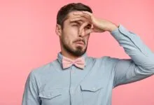 Man pinching nose with disgusted expression on pink background.