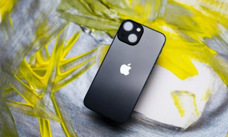 Black iPhone with dual camera on a colorful painted background.