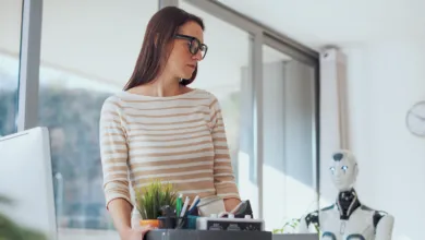 Woman carrying box with office items, robot in background.