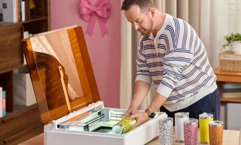 Man places decorated tumbler into open xTool M2 laser engraver.