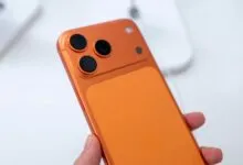 Close-up of orange smartphone with three camera lenses on the back.