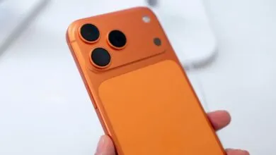 Close-up of orange smartphone with three camera lenses on the back.