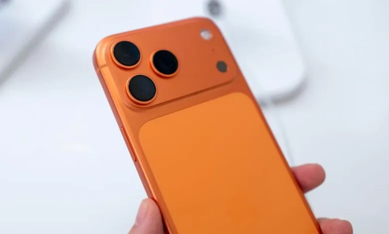Close-up of orange smartphone with three camera lenses on the back.