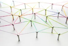 Network of colorful strings connecting pins on a white surface.
