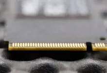 Close-up of a gray SSD card with gold connectors on a textured surface.