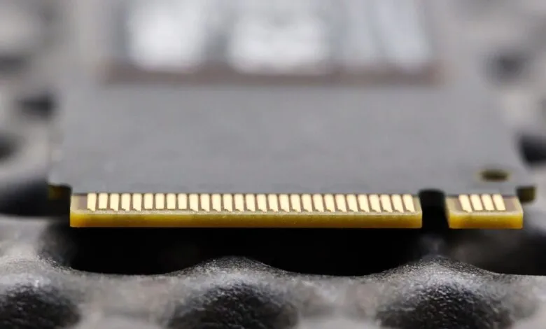 Close-up of a gray SSD card with gold connectors on a textured surface.