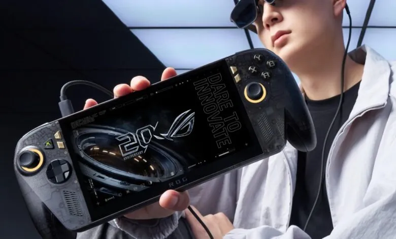 Person holding ASUS ROG Ally X handheld gaming console, screen displaying 20th anniversary logo.