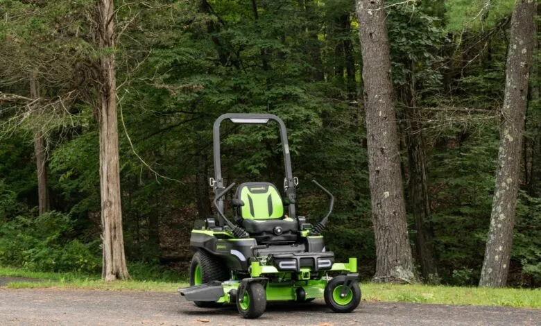 Greenworks zero-turn lawn mower parked on an asphalt driveway near lush green trees.