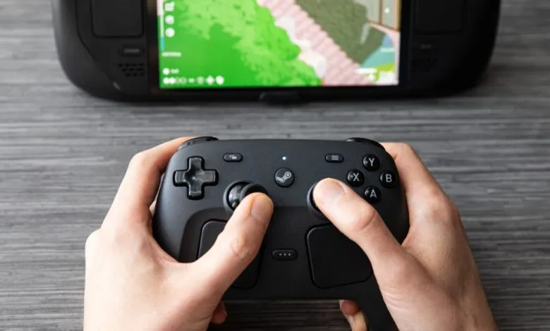 Close-up of hands holding a black Steam Controller with a gaming device display in the background.
