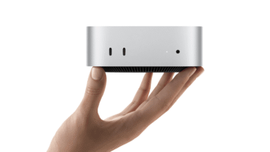 A hand holds the compact Apple Mac mini, showcasing its small silver chassis and front ports.