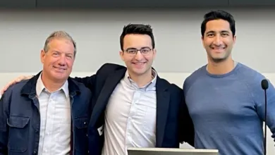 Three men smiling together, with arms around each other in a modern indoor setting.