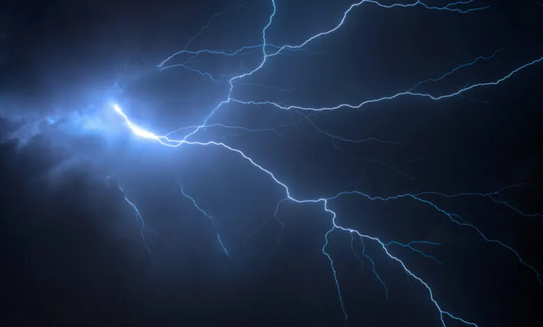 Vibrant blue lightning flashes across a dark, stormy night sky.