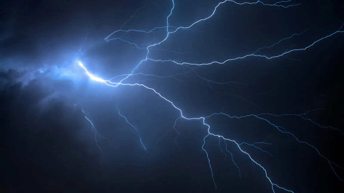 Vibrant blue lightning flashes across a dark, stormy night sky.