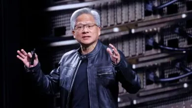 NVIDIA CEO Jensen Huang speaks on stage wearing his signature black leather jacket in front of server racks.