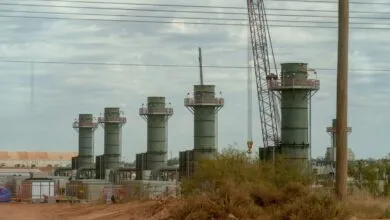 Industrial construction site with several green vertical cylindrical towers and a large crane under a cloudy sky.