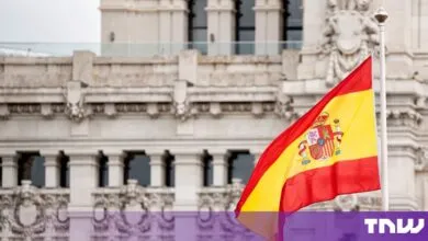 The flag of Spain waving proudly in front of a majestic, ornate stone government building.