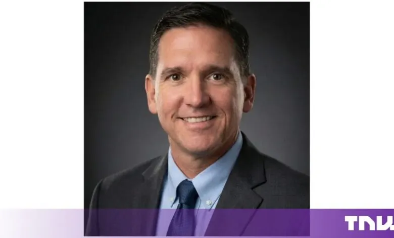 Professional headshot of a smiling man in a suit against a dark background