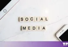 Scrabble tiles spelling out SOCIAL MEDIA on a white marble surface with devices