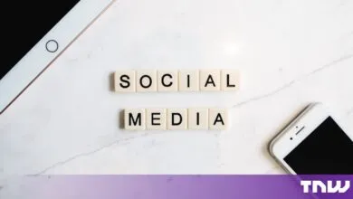 Scrabble tiles spelling out SOCIAL MEDIA on a white marble surface with devices
