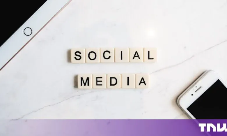 Scrabble tiles spelling out SOCIAL MEDIA on a white marble surface with devices