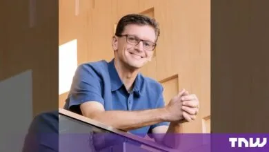 Chris Malone smiling while leaning against a railing in front of a wooden wall.
