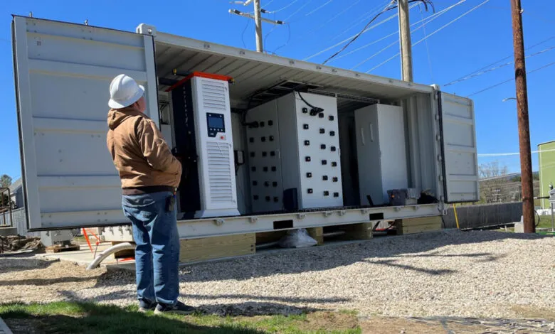 Worker in hard hat and brown jacket inspects deployed solid-state transformer in a shipping container.