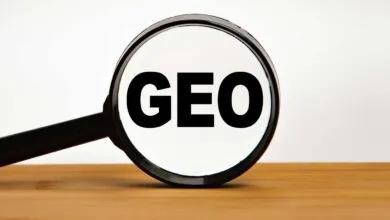 Magnifying glass focusing on the bold black word GEO on a white background over wooden surface.