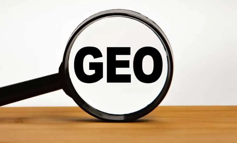 Magnifying glass focusing on the bold black word GEO on a white background over wooden surface.