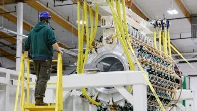 Engineer stands on ladder beside complex cylindrical Pacific Fusion pulser prototype in facility.