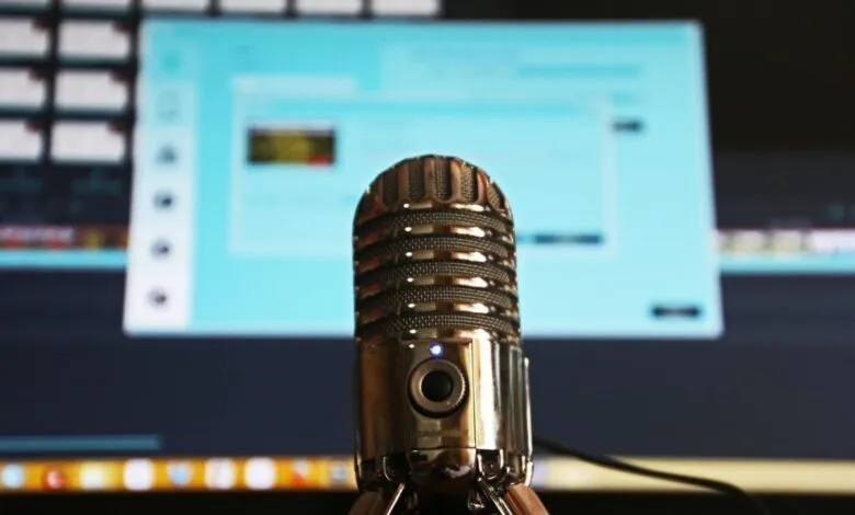 Close-up of a vintage-style silver microphone against a blurred computer screen backdrop.