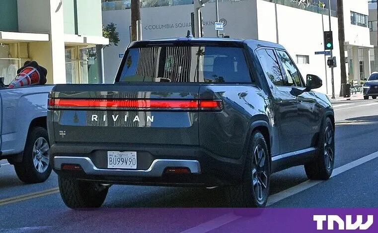 Dark green Rivian electric truck parked on a sunny city street.