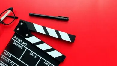 Black and white film clapperboard with glasses and a pen on a vibrant red background.