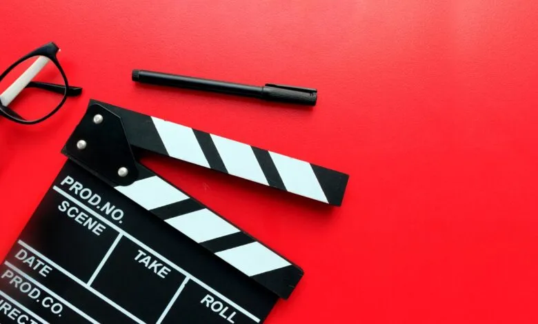 Black and white film clapperboard with glasses and a pen on a vibrant red background.