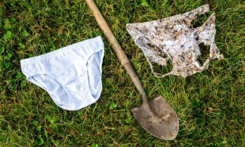 A clean pair of white underpants and a heavily decomposed pair resting on green grass next to a garden shovel.