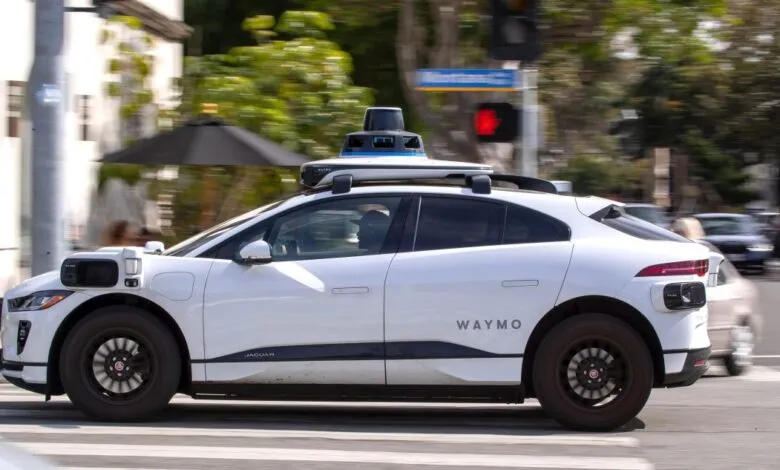 White Waymo autonomous Jaguar I-PACE drives on a city street with motion blur background.
