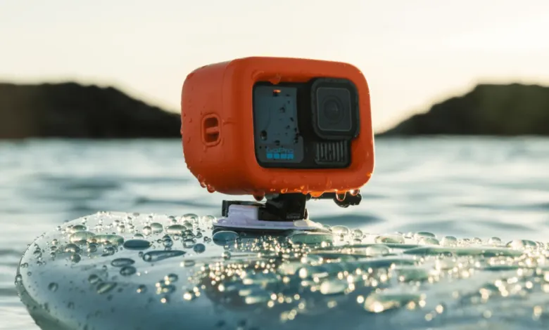 Orange GoPro action camera mounted on a wet surfboard floating on the water.