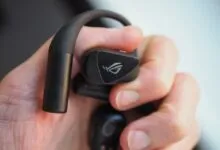 Close-up of a person holding black Asus ROG Cetra wireless earbuds with an over-ear hook design.