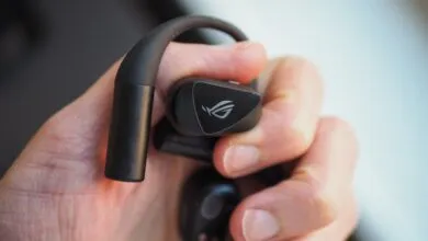 Close-up of a person holding black Asus ROG Cetra wireless earbuds with an over-ear hook design.