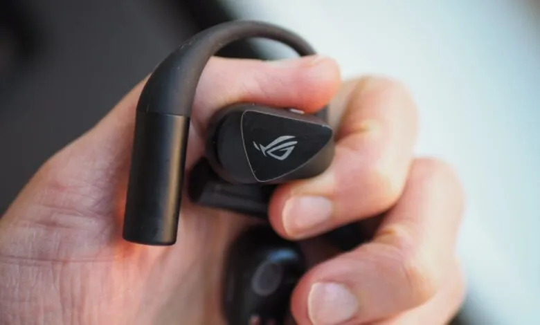 Close-up of a person holding black Asus ROG Cetra wireless earbuds with an over-ear hook design.