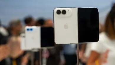 Close-up of a white and black foldable smartphone displayed on a metal stand at a tech event.