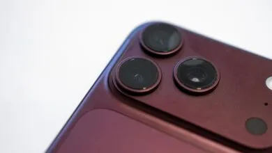Close-up of a dark burgundy iPhone triple camera module and rear glass panel against white.