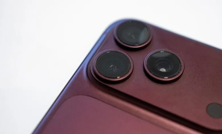 Close-up of a dark burgundy iPhone triple camera module and rear glass panel against white.