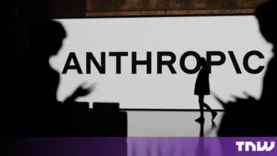Silhouette of a person walking past a large screen displaying the Anthropic logo in a modern space.