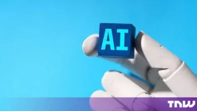 A robotic hand holding a blue block with the letters AI printed in cyan against a bright blue background