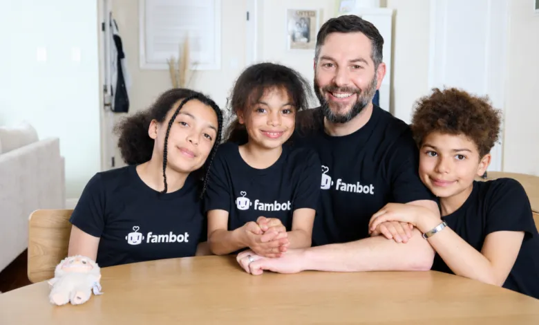 A smiling man and three children sitting at a wooden table wearing matching Fambot t-shirts