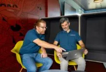 Two men in blue polo shirts collaborating on a laptop in a vibrant modern office space.