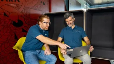 Two men in blue polo shirts collaborating on a laptop in a vibrant modern office space.