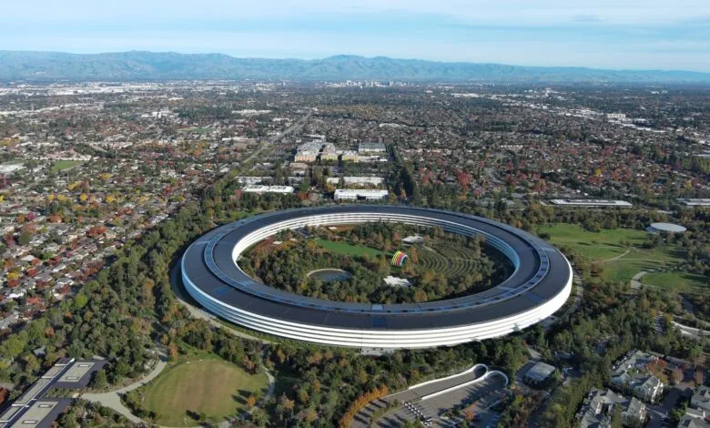 Aerial view of Apple Park campus featuring the massive circular ring building surrounded by trees and mountains.