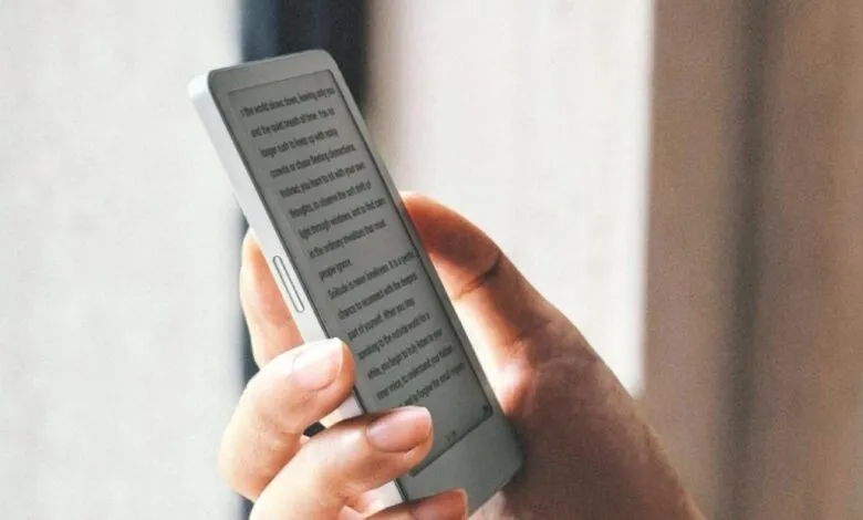 Person holding a compact electronic e-reader device displaying text on its screen.