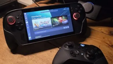 A handheld gaming console displaying Xbox Cloud Gaming on a wooden desk with a wireless controller.